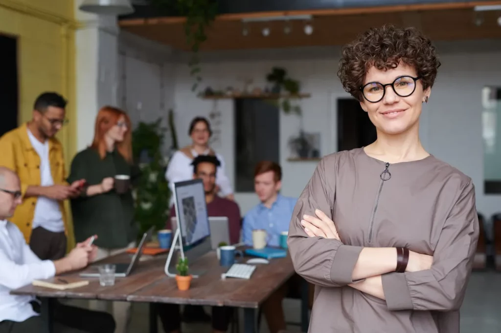 Woman with glasses in focus, group of other adults slightly out of focus around a computer at an upskilling meeting