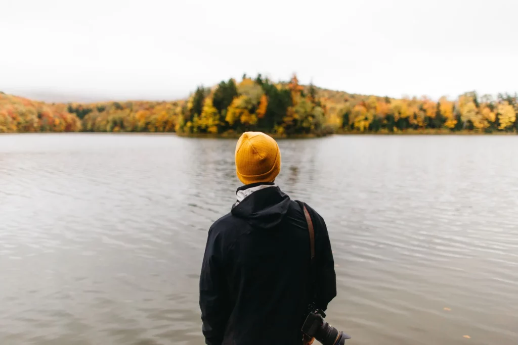 Photographer standing at the edge of a lake looking at foliage in Vermont