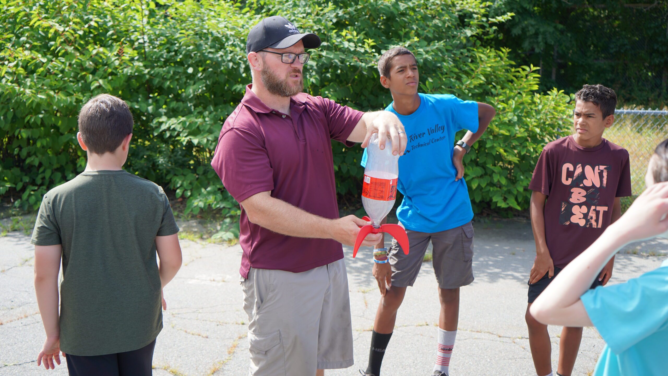 A male teacher with four students holds a water bottle rocket in his hands outside
